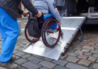 A photo of a wheelchair user being pushed up a wheelchair ramp.